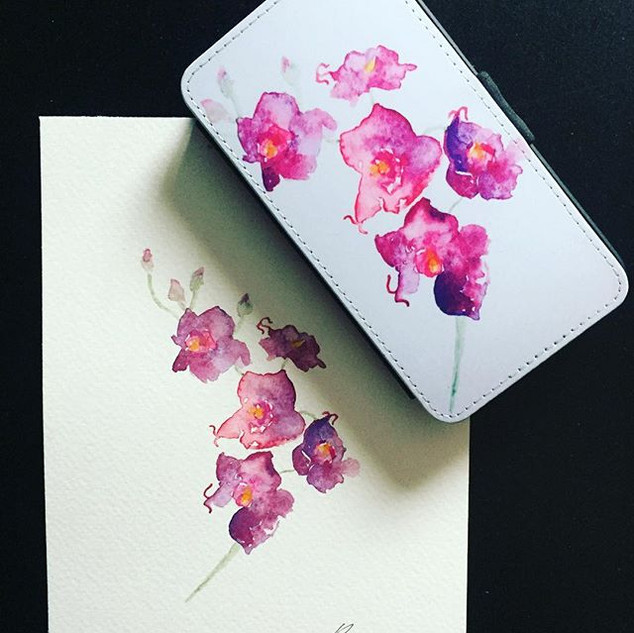 A watercolor painting of pink and purple orchid flowers on paper beside a phone case with a matching floral design